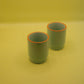 Two green ceramic cups with orange rims on a yellow background