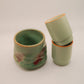 Two green ceramic cups stacked on a white background
